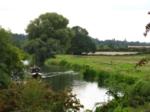 A narrowboat makes its way along the River Nene with a Nene Valley Railway train behind